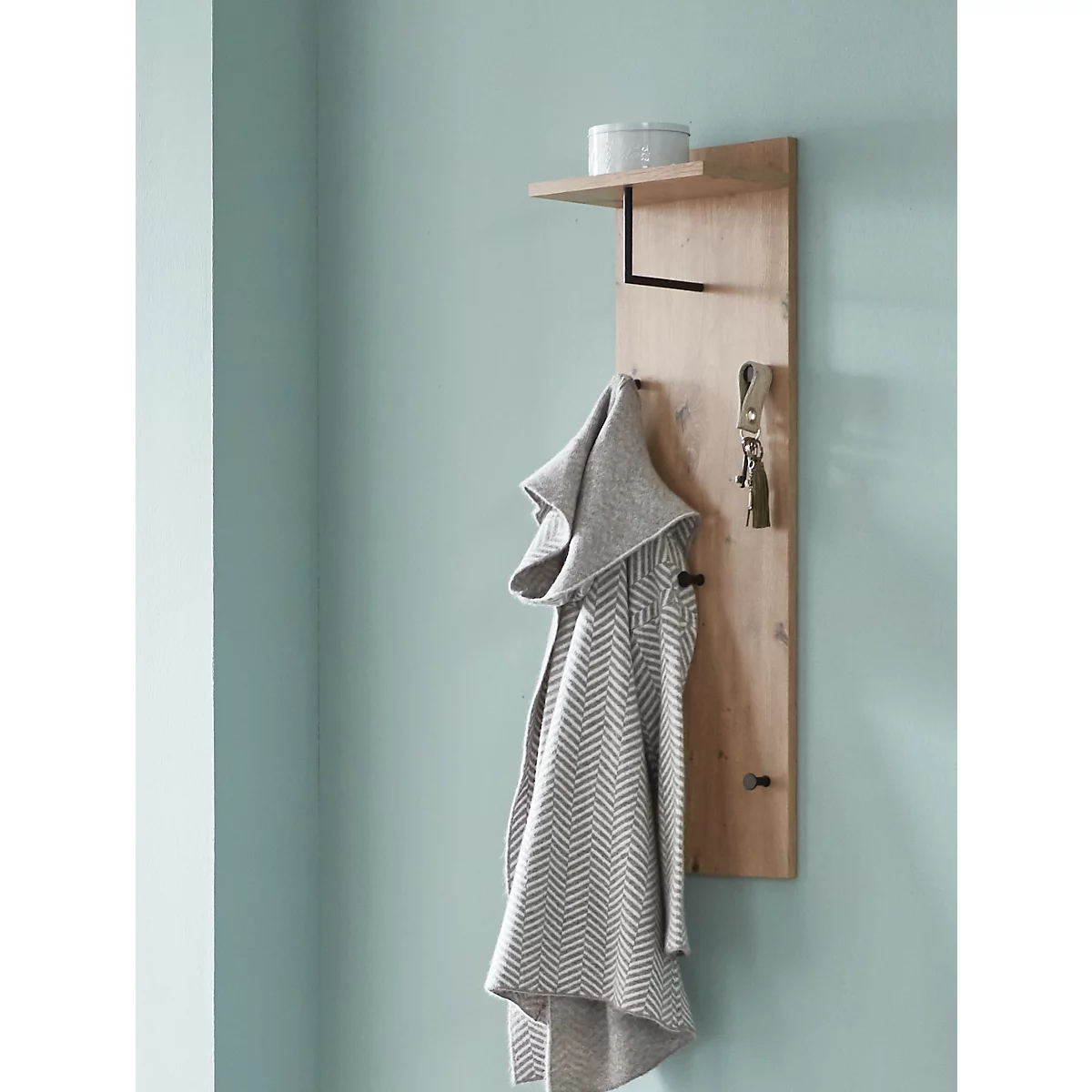 Holzwand mit Regal, Kleiderhaken, Schlüsselanhänger und grauer Jacke. Auf dem Regal steht ein weißer Behälter.