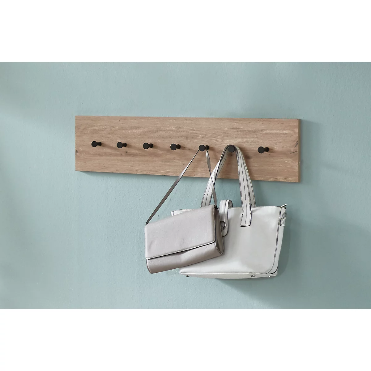 Garderobenleiste aus Holz mit schwarzen Haken, an denen zwei Handtaschen hängen.