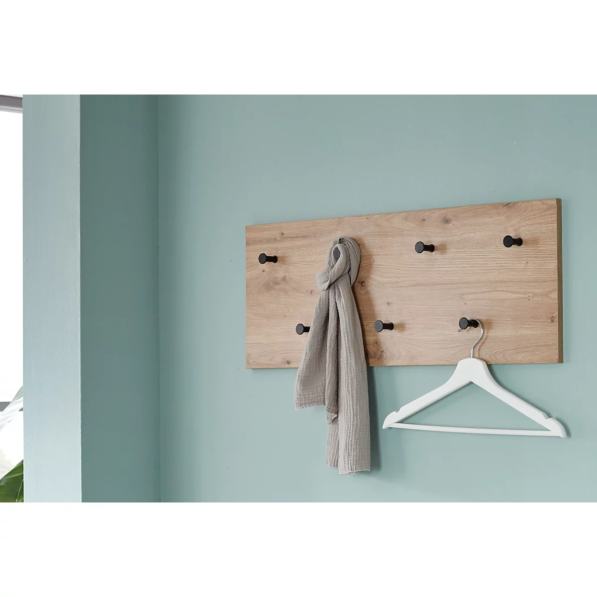 Holzgarderobe an hellblauer Wand. Ein grauer Schal hängt an der Garderobe. Darunter ein weißer Kleiderbügel.