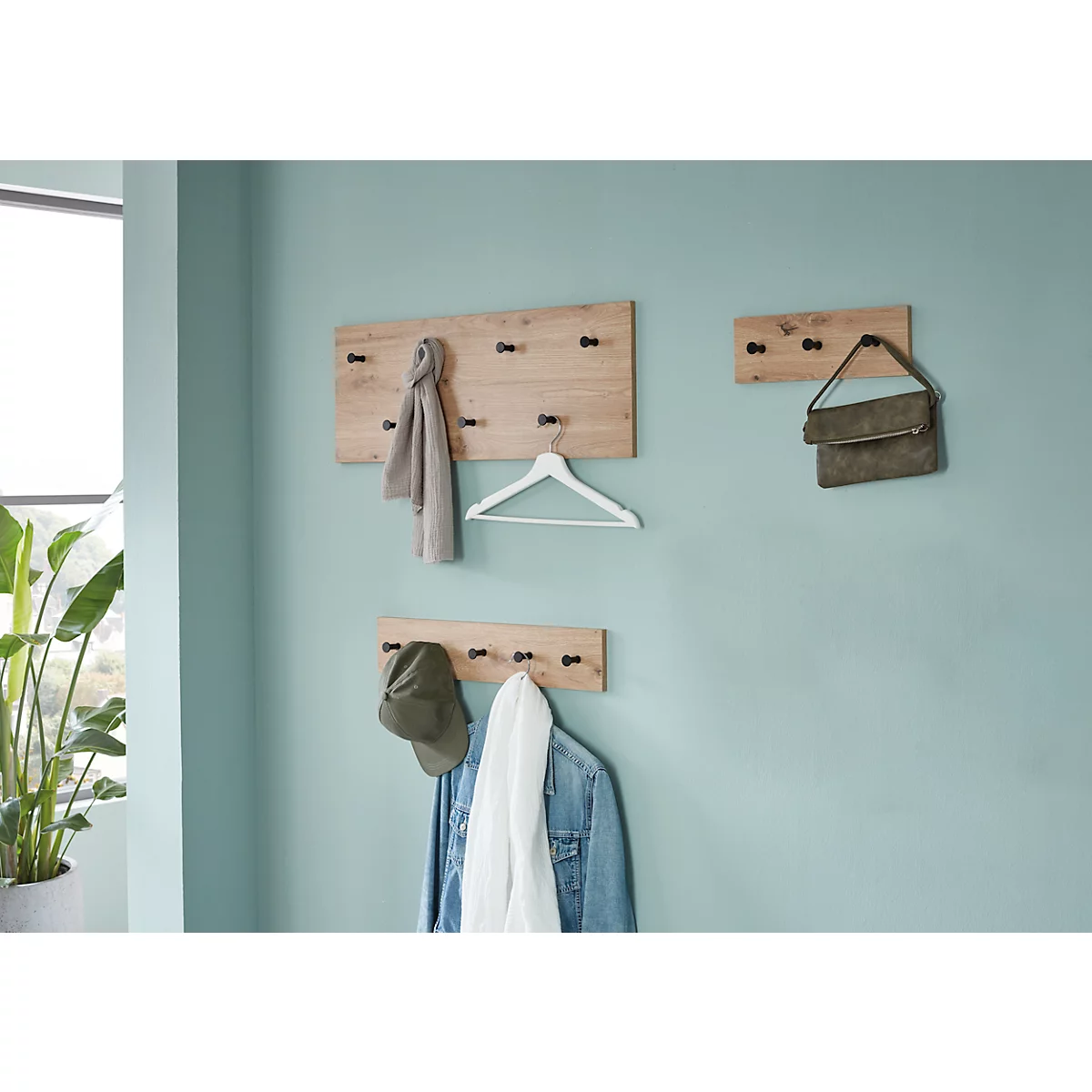 Holzgarderobe mit Kleidung und Accessoires an hellblauer Wand.