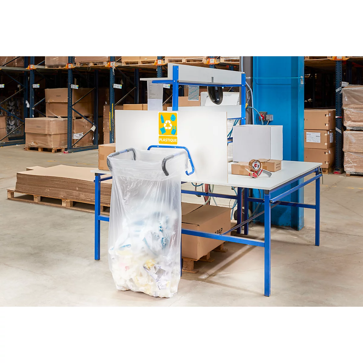 Arbeitsplatz in einer Lagerhalle. Eine transparente Plastiktüte hängt an einem Tisch. Auf dem Tisch befinden sich weiteres Material.