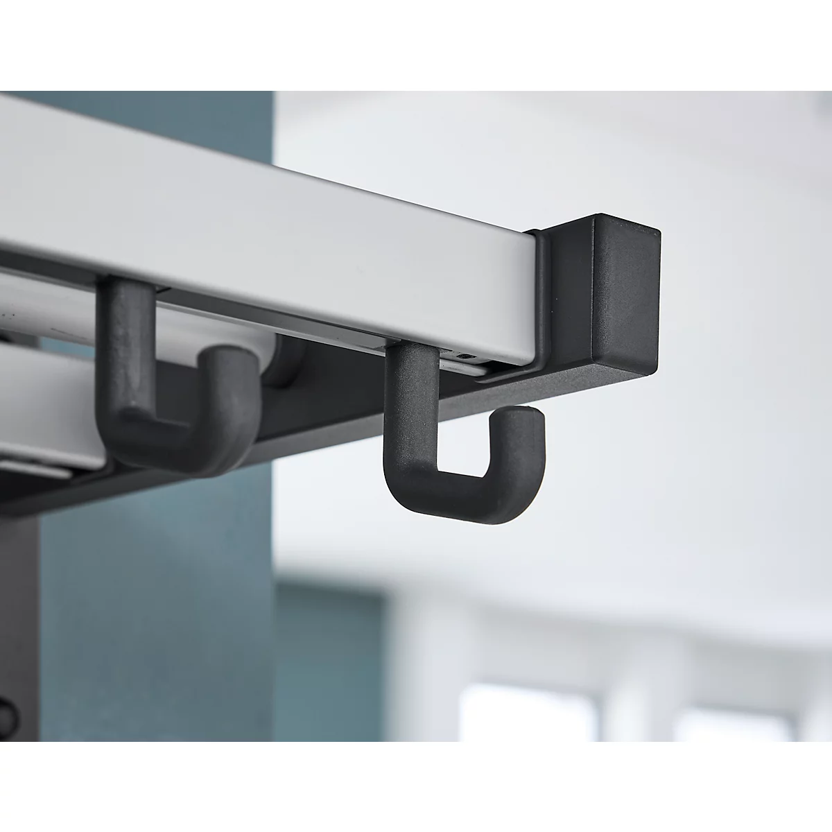 Close-up van zwarte haken die onder een witte rail hangen.