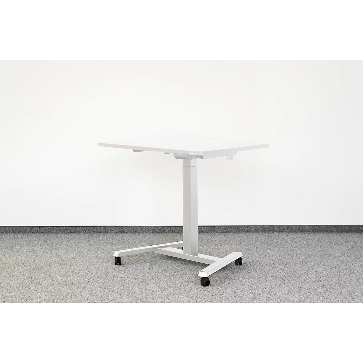 In hoogte verstelbaar grijs bureau tegen witte muur. Hij staat op wielen.
