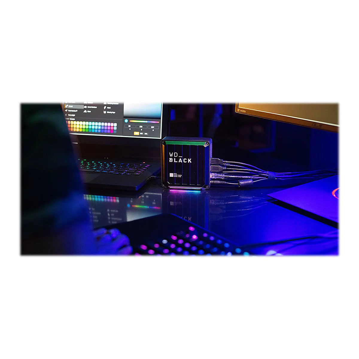 Auf einem Schreibtisch mit RGB-Beleuchtung steht ein WD-Black-Laufwerk. Ein Spieler ist am Computer aktiv.