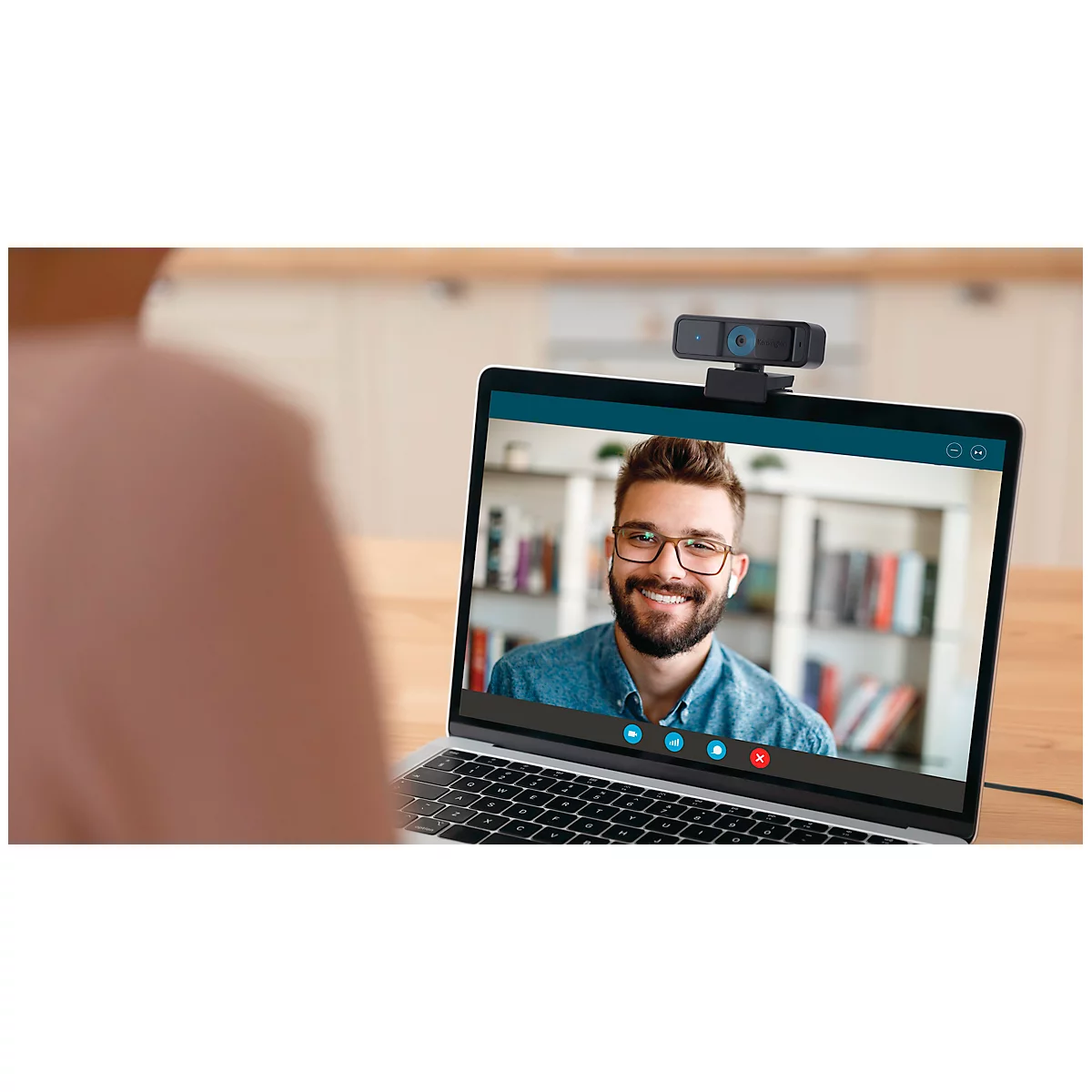 Close-up van een laptop met videovergadering. Een lachende man op het scherm, een persoon op de voorgrond, een webcam bovenop.