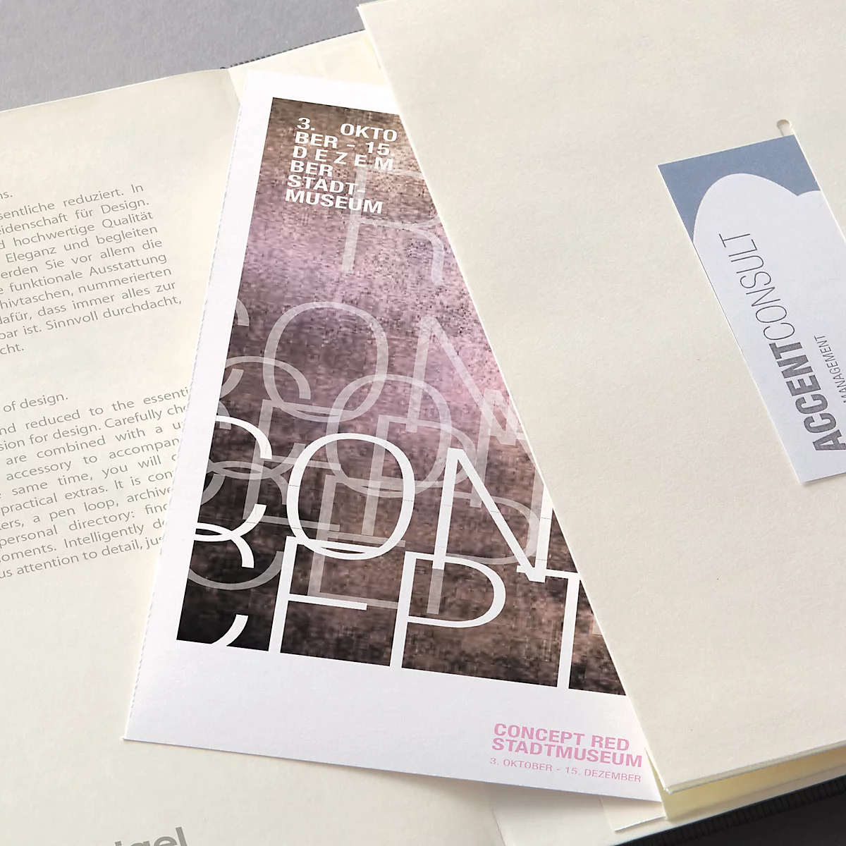 Een driehoekige brochure met het woord "CONCEPT" en teksten in het Duits. Daarnaast een visitekaartje met "ACCENTCONSULT".
