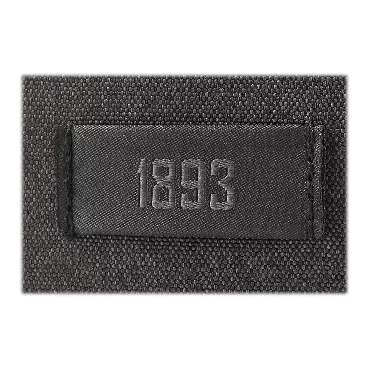 Detailaufnahme einer rechteckigen Plakette mit der Zahl 1893 in geprägter Schrift auf einem texturierten Stoffhintergrund.