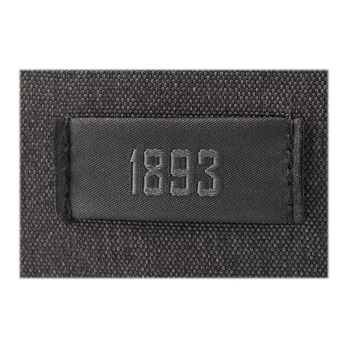 Detailaufnahme eines dunkelgrauen Textilstücks mit dem aufgestickten Jahr „1893“ auf einem eingenähten Etikett.