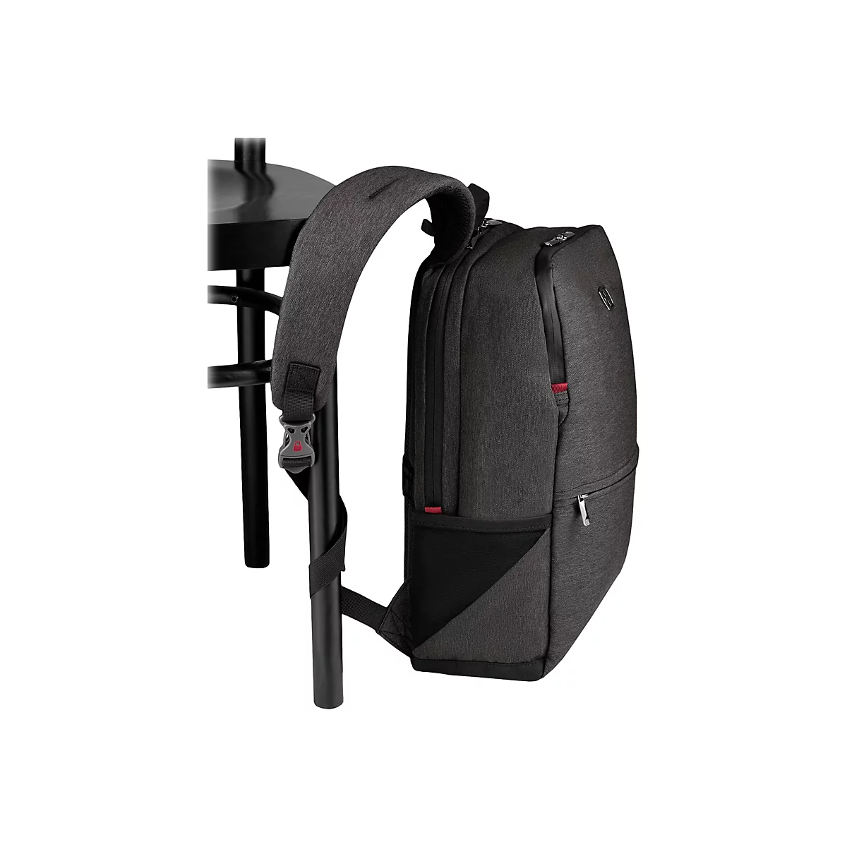 Dunkelgrauer Rucksack, an einer schwarzen Stuhllehne befestigt. Details: Reißverschlüsse, rote Akzente, Textur.