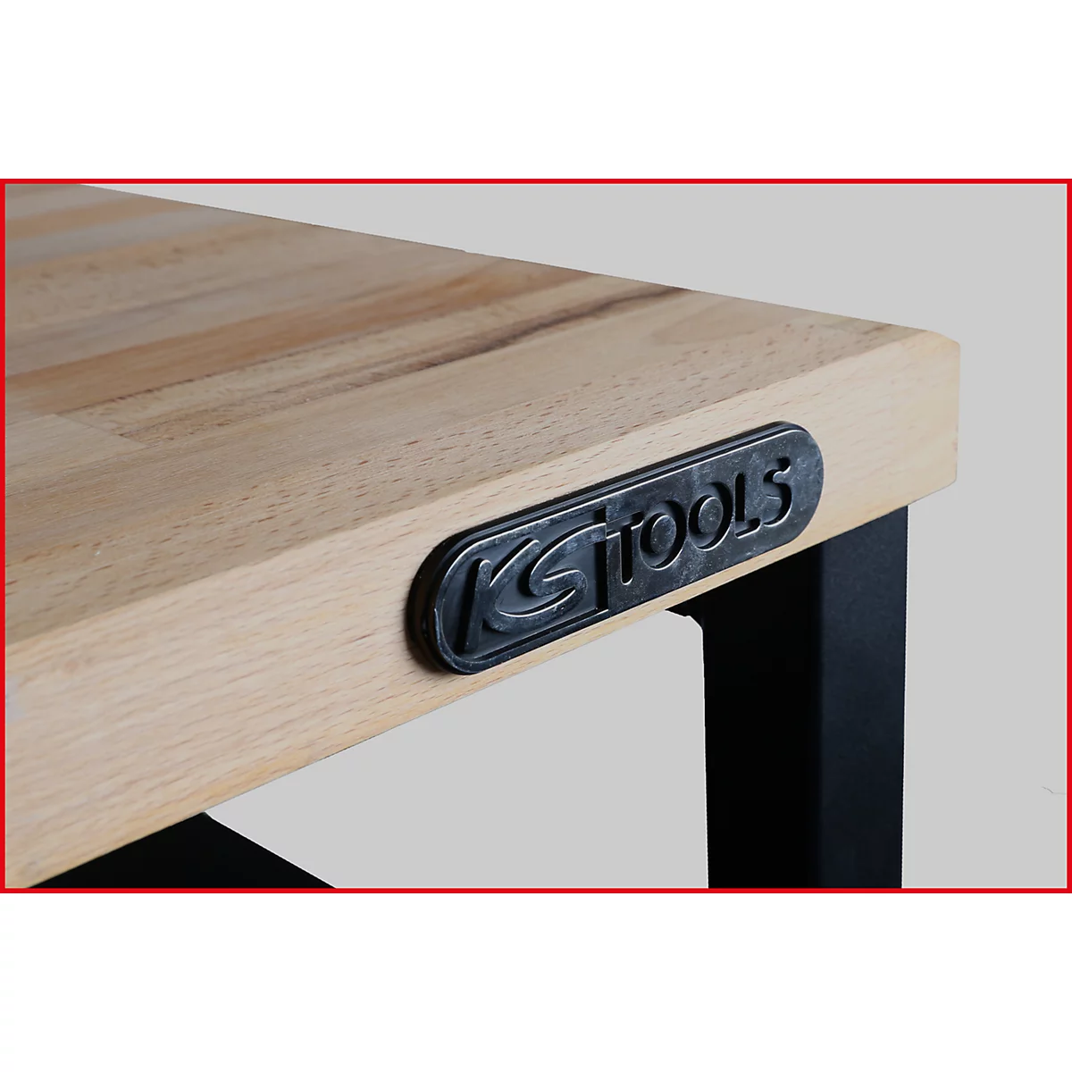 Nahaufnahme einer Werkbank-Ecke. Holzplatte mit Logo-Schild 'KS TOOLS' und schwarzem Bein.
