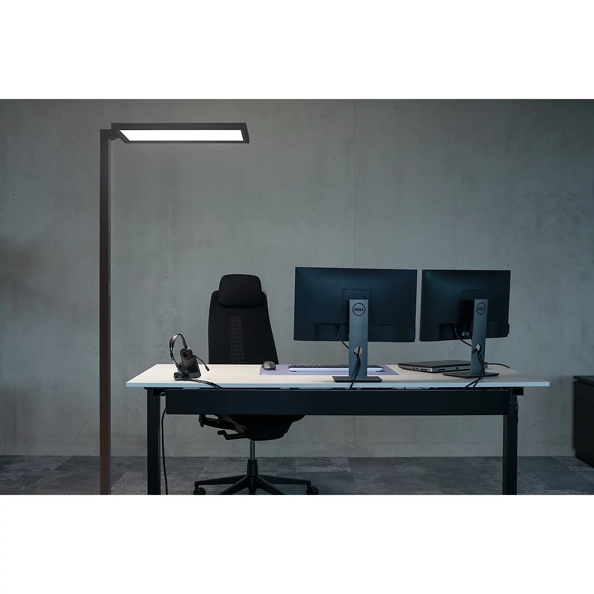 Kantoor met bureau, monitoren, stoel en staande lamp. Neutrale achtergrond.