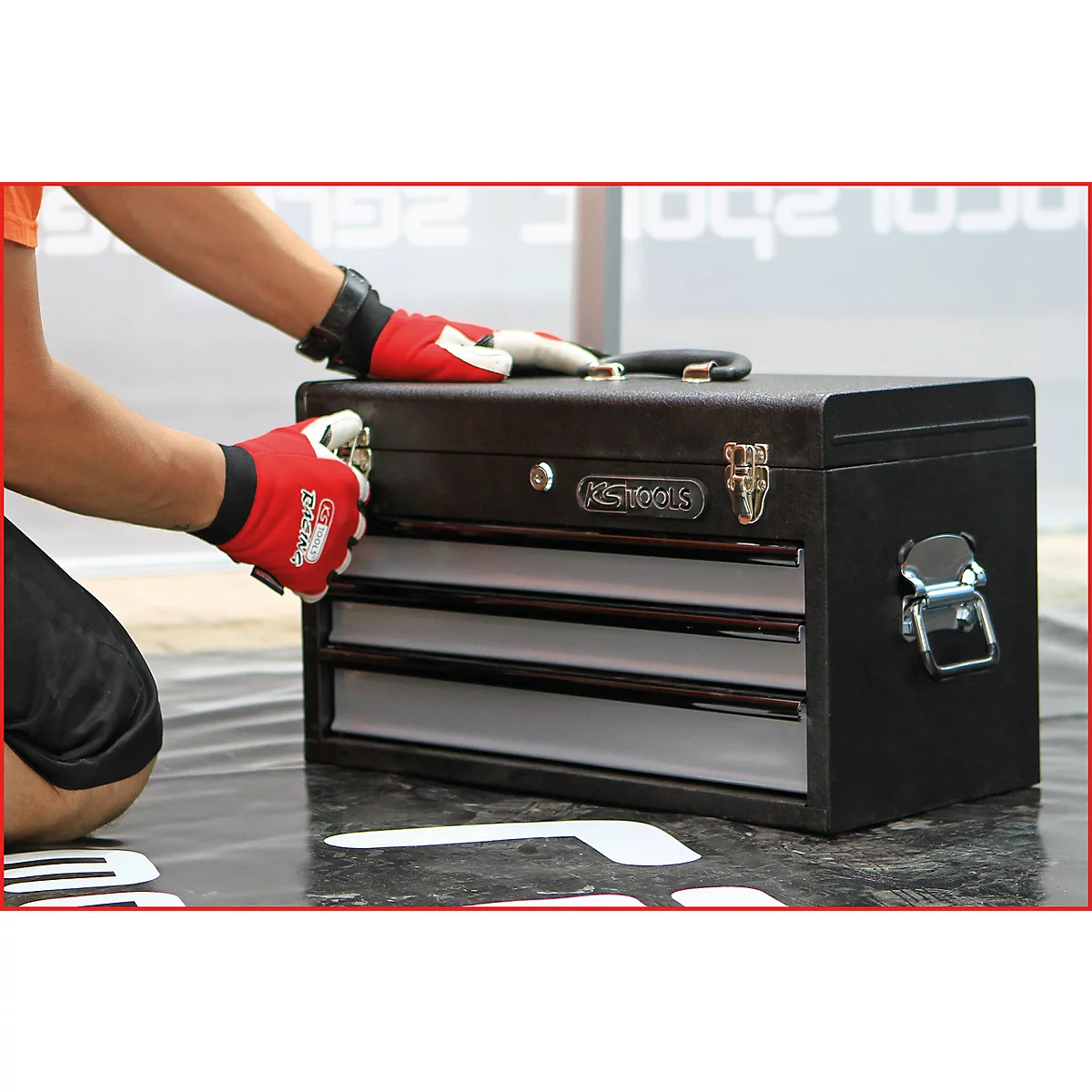 Person öffnet Werkzeugkiste. Schwarze Kiste mit silbernen Verschlüssen, roten Handschuhen.