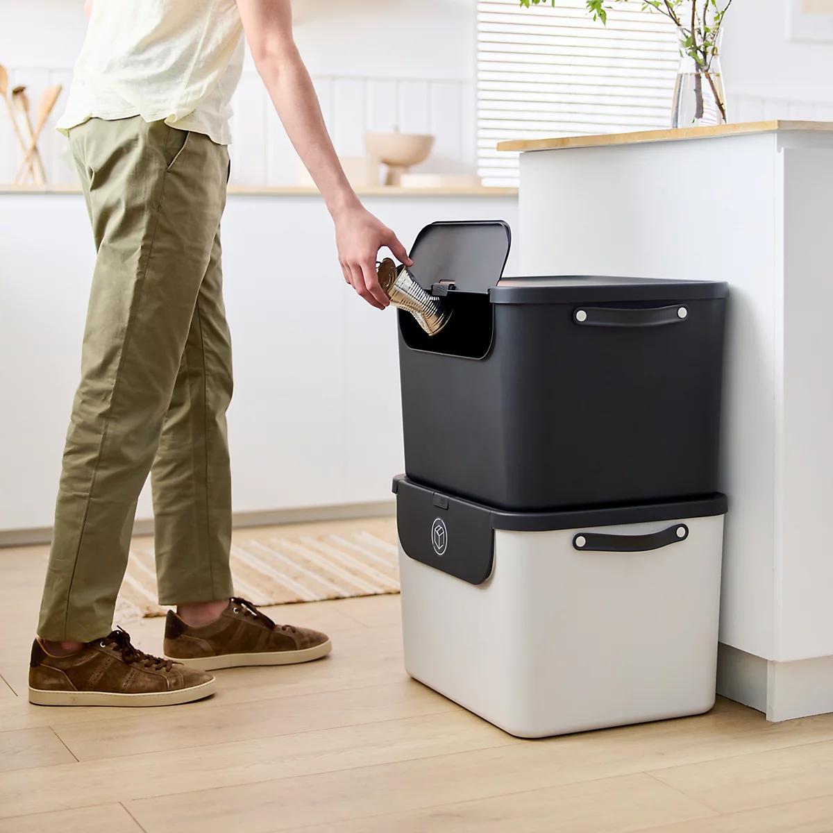 Graue Aufbewahrungsbox mit Deckel und Henkeln. Der Deckel ist teilweise geöffnet. Rechts daneben eine Aussparung.