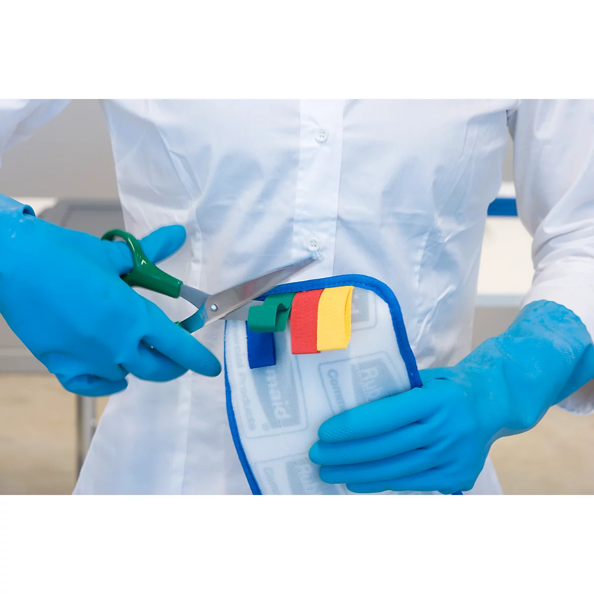 Person in white lab coat and blue gloves cuts colored tabs off a piece of fabric with scissors.