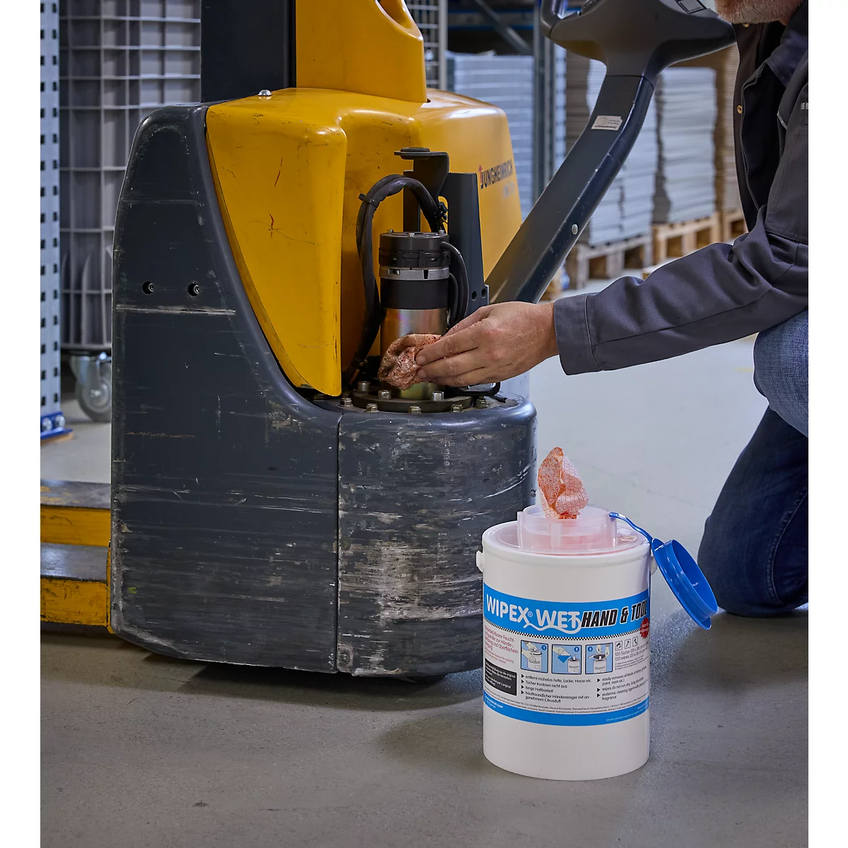 Een man die een vorkheftruck schoonmaakt met een natte doek. Daarnaast staat een emmer "Wipex Wet Wipes".