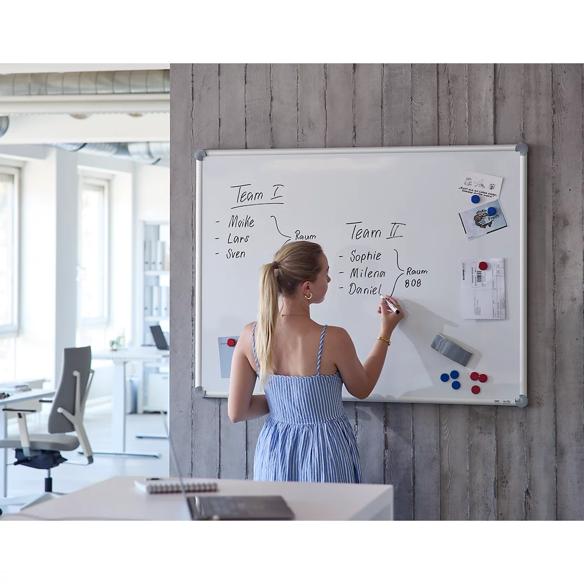 Eine Frau schreibt mit einem Stift auf ein Whiteboard in einem modernen Büro.