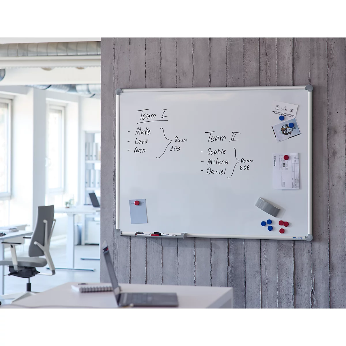 Ein Whiteboard an einer grauen Betonwand mit handgeschriebenen Teamplänen und Notizen.