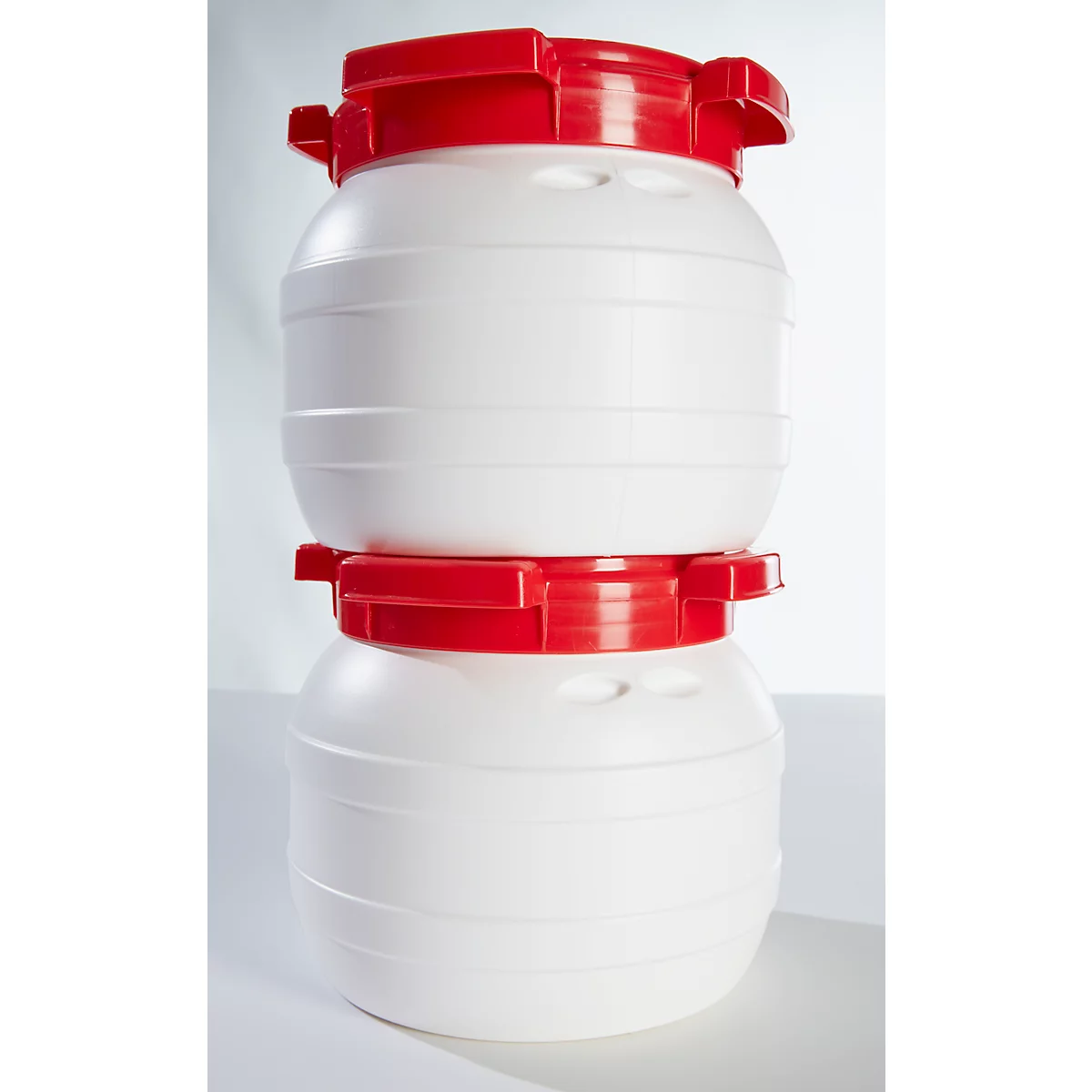 Two white barrels with red lids stacked on top of each other. The barrels have a cylindrical body with horizontal grooves.