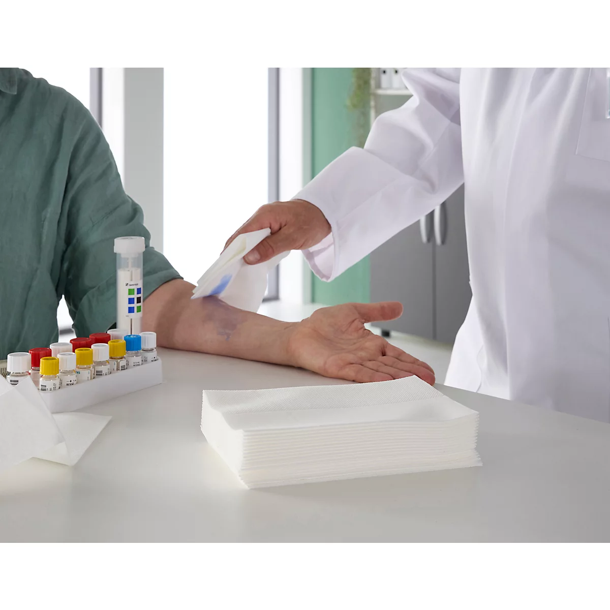 Arts veegt arm af na bloedafname. Daarnaast reageerbuisjes en testflesjes.