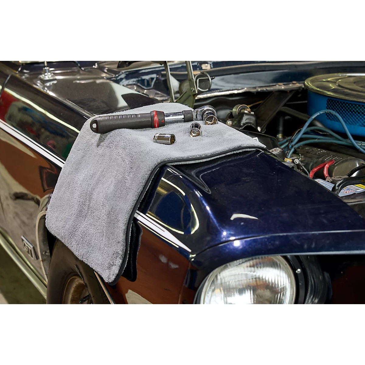 Des outils, dont une clé et des douilles, sont posés sur un chiffon gris sur un garde-boue de voiture bleu.