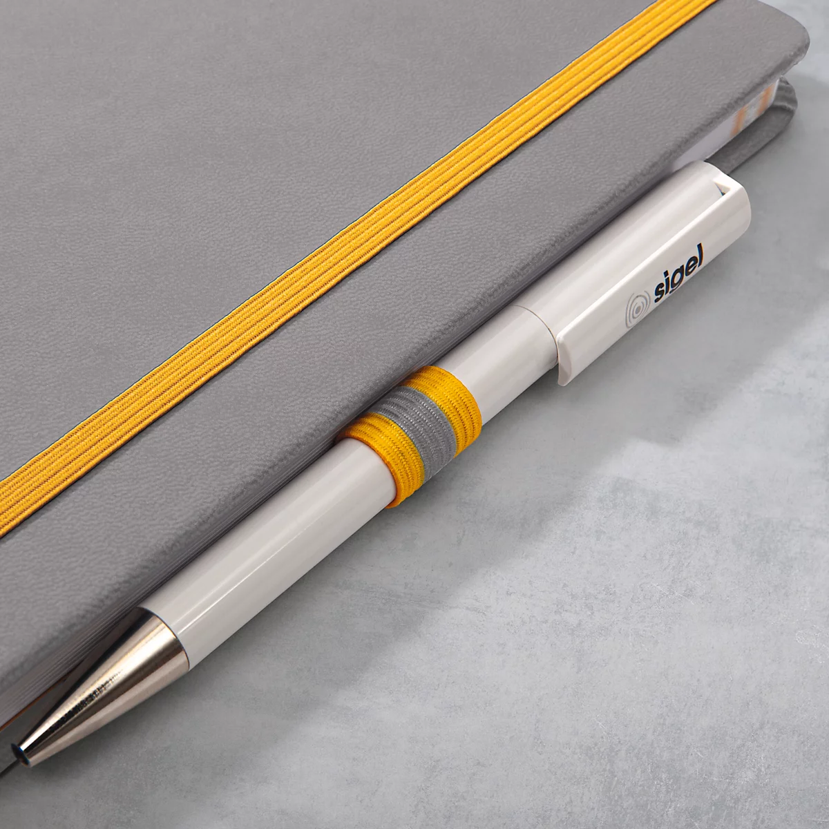 Weißer Stift mit gelbem Ring, der in einem grauen Notizbuch mit gelben Gummibändern liegt.
