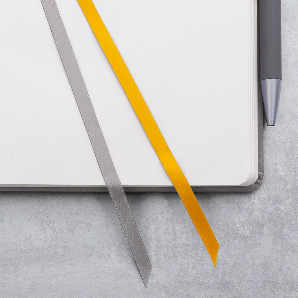 Notizbuch mit zwei Lesezeichen, einem grauen und einem gelben. Ein Stift liegt am Rand.