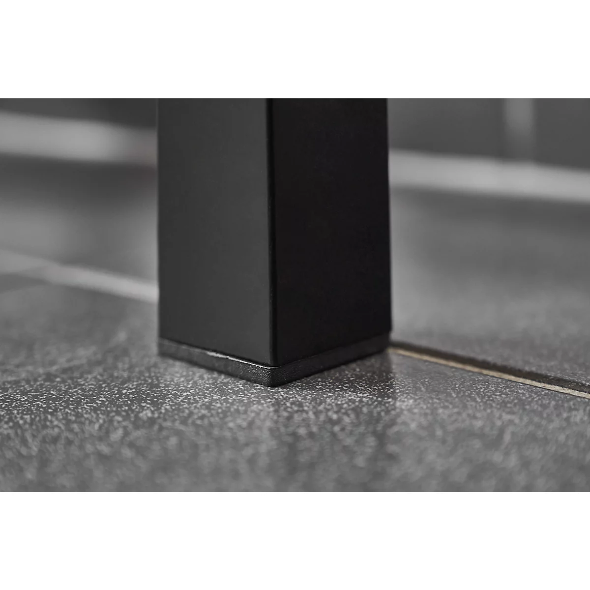 Close-up of a black table leg corner on a gray tiled floor.