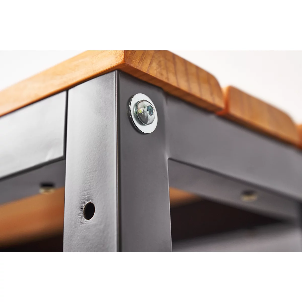 Close-up of a table construction: Wooden top on a dark metal frame, screwed with silver nuts.