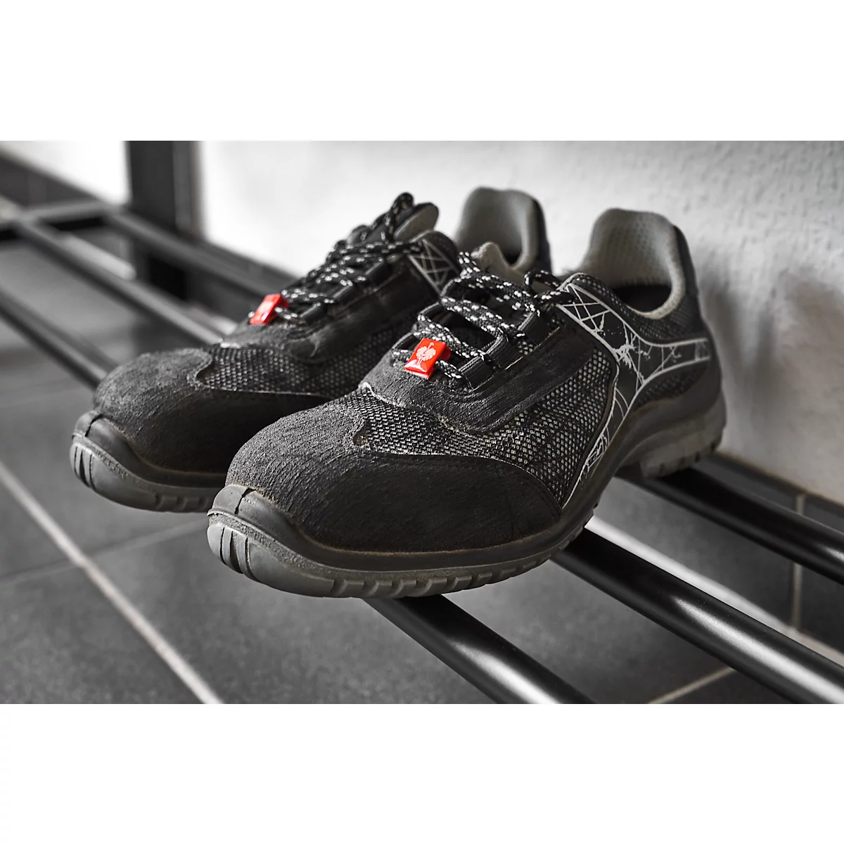 Black safety shoes with red details are on a black shelf.