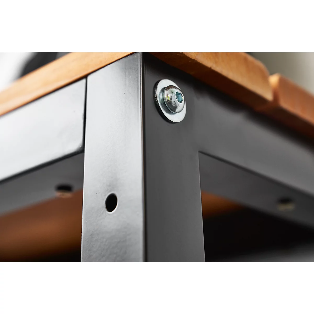 Close-up of a corner of a black metal table. Wooden top, screwed together with silver screws.