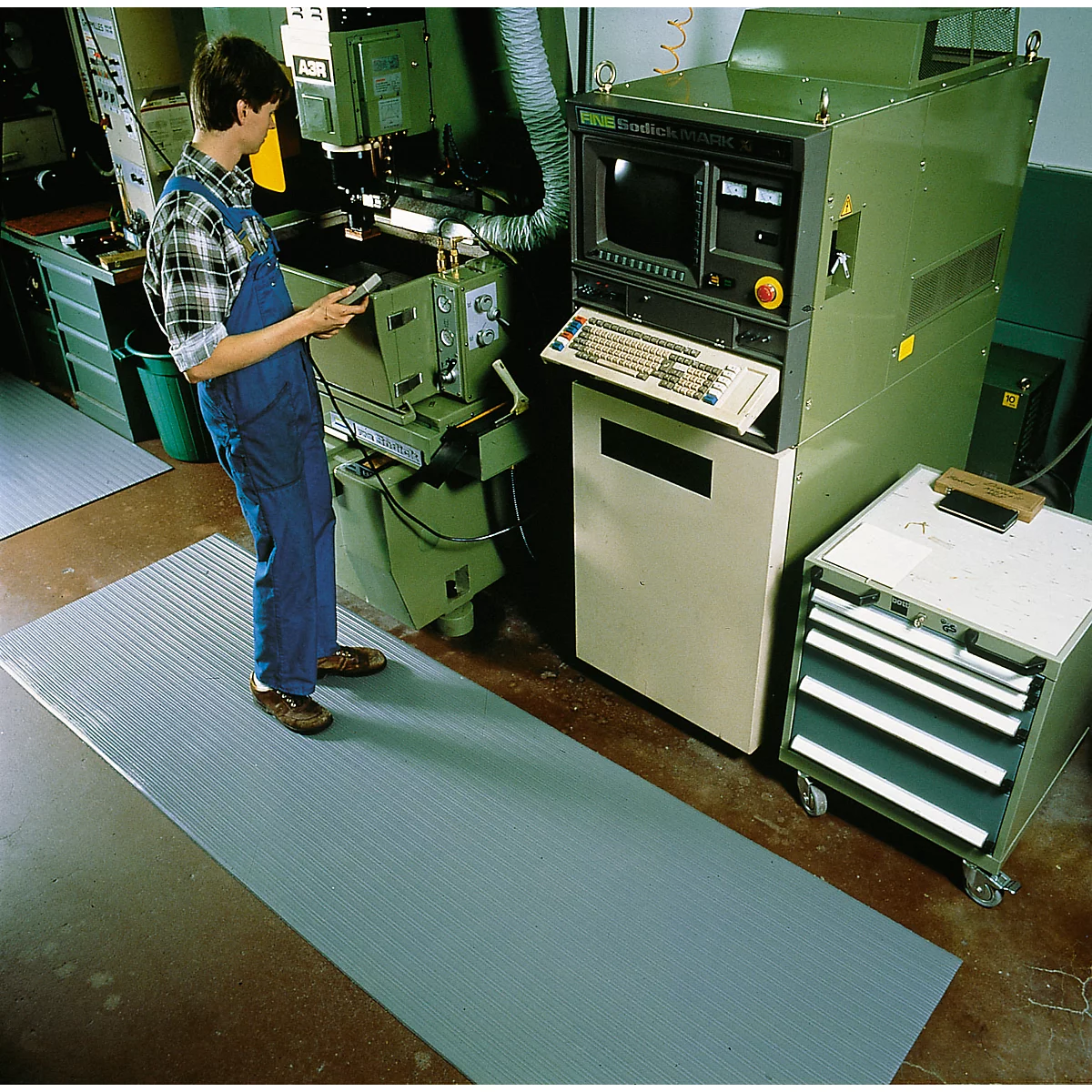 Man in blue overalls operating machine on a gray mat.