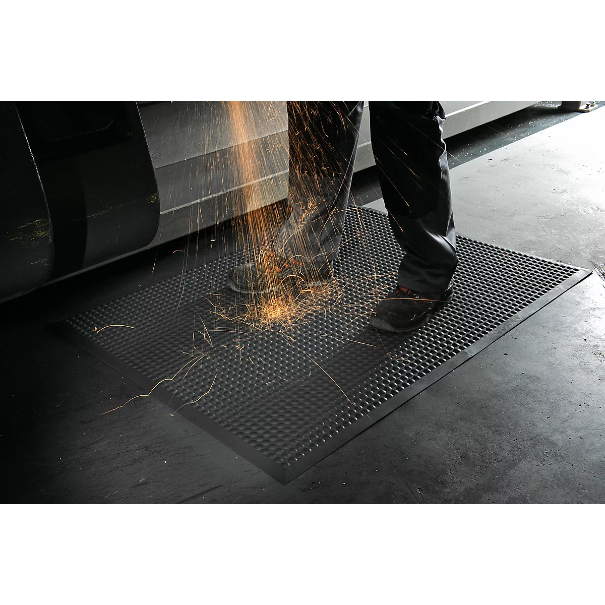 Man stands on a black, studded mat. Sparks are flying during the work.