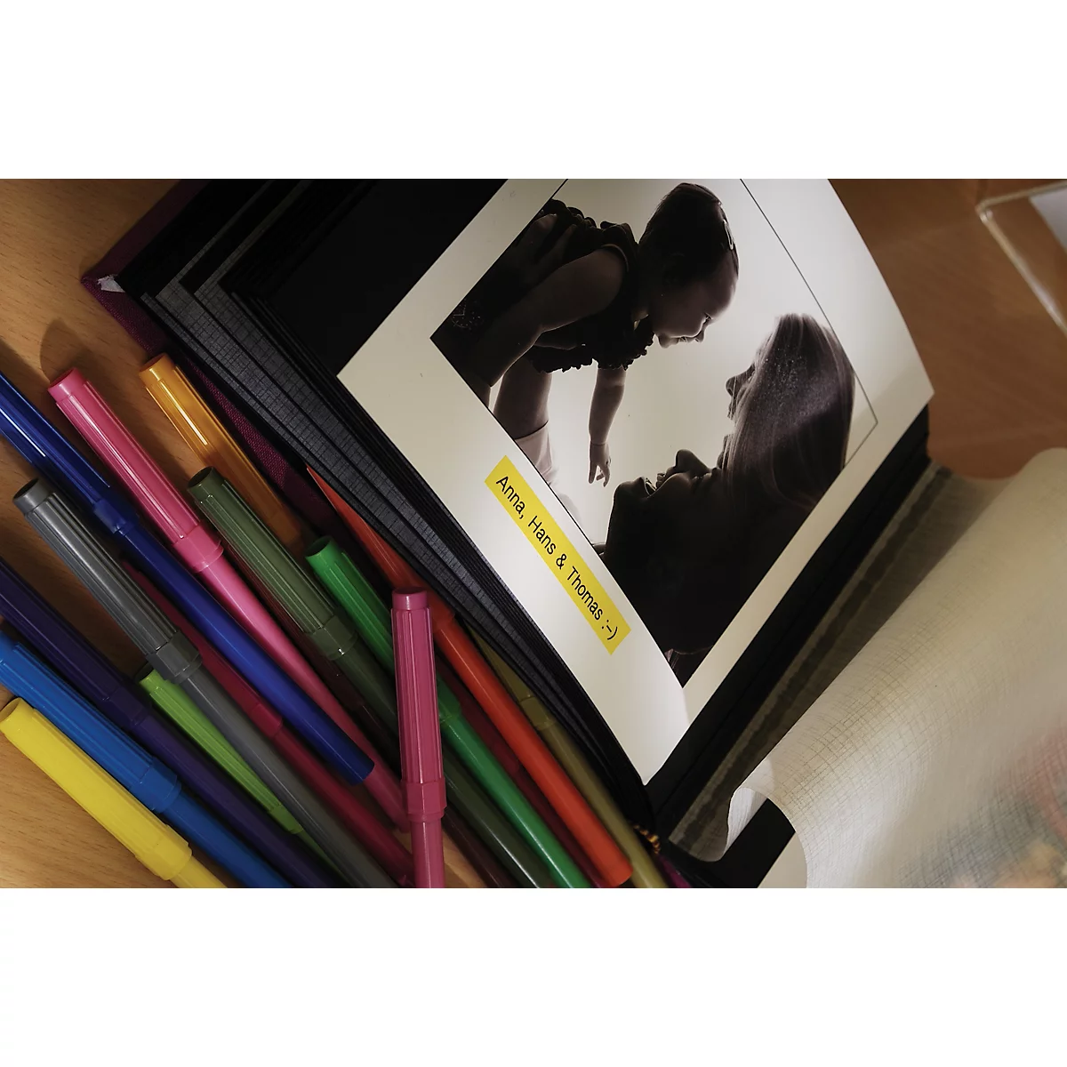 Photo album with black and white photo, colorful pens next to it. On yellow sign: Anna, Hans & Thomas :)