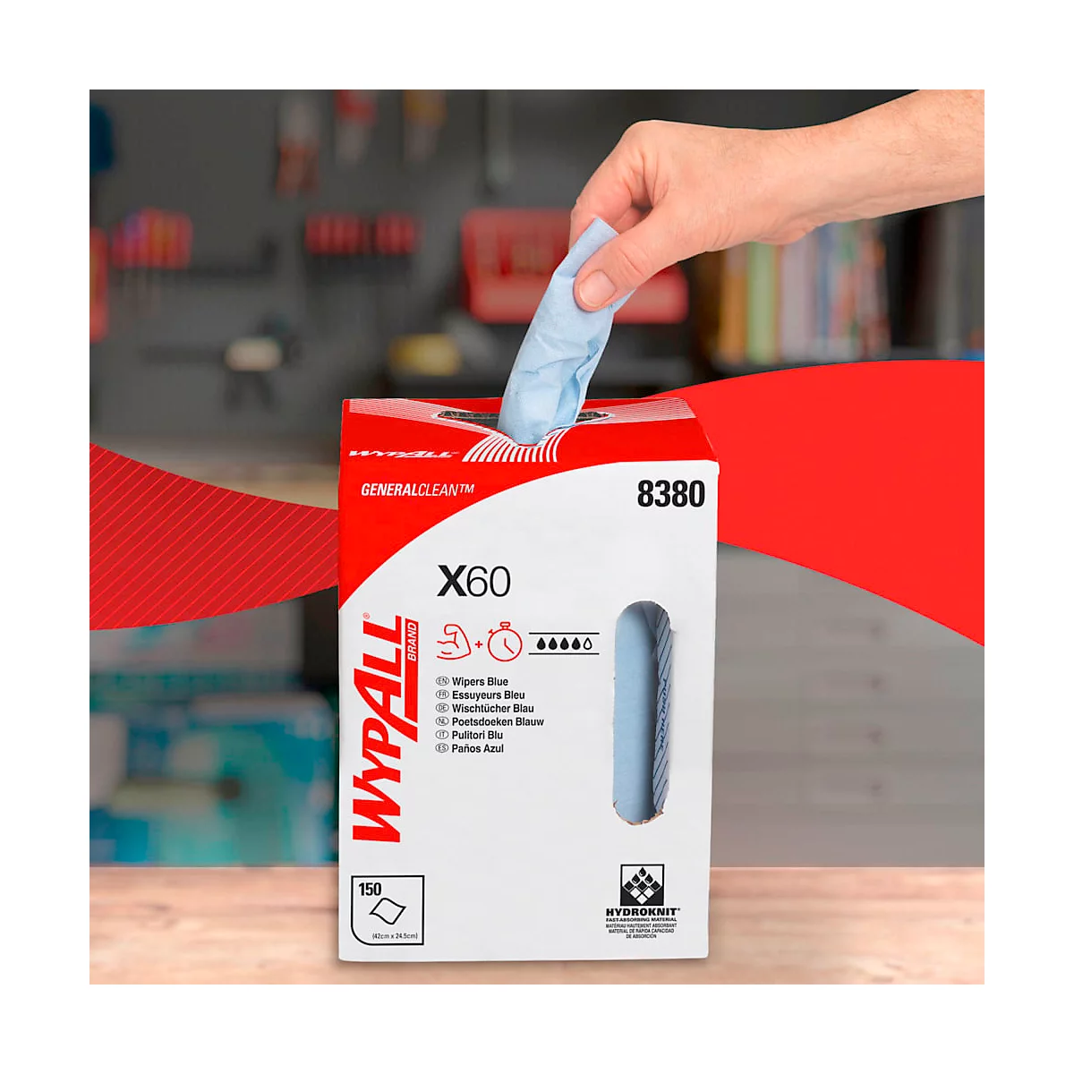 Een hand trekt een blauwe doek uit een rode en witte WYPALL dispenser, tegen een achtergrond van gereedschap.