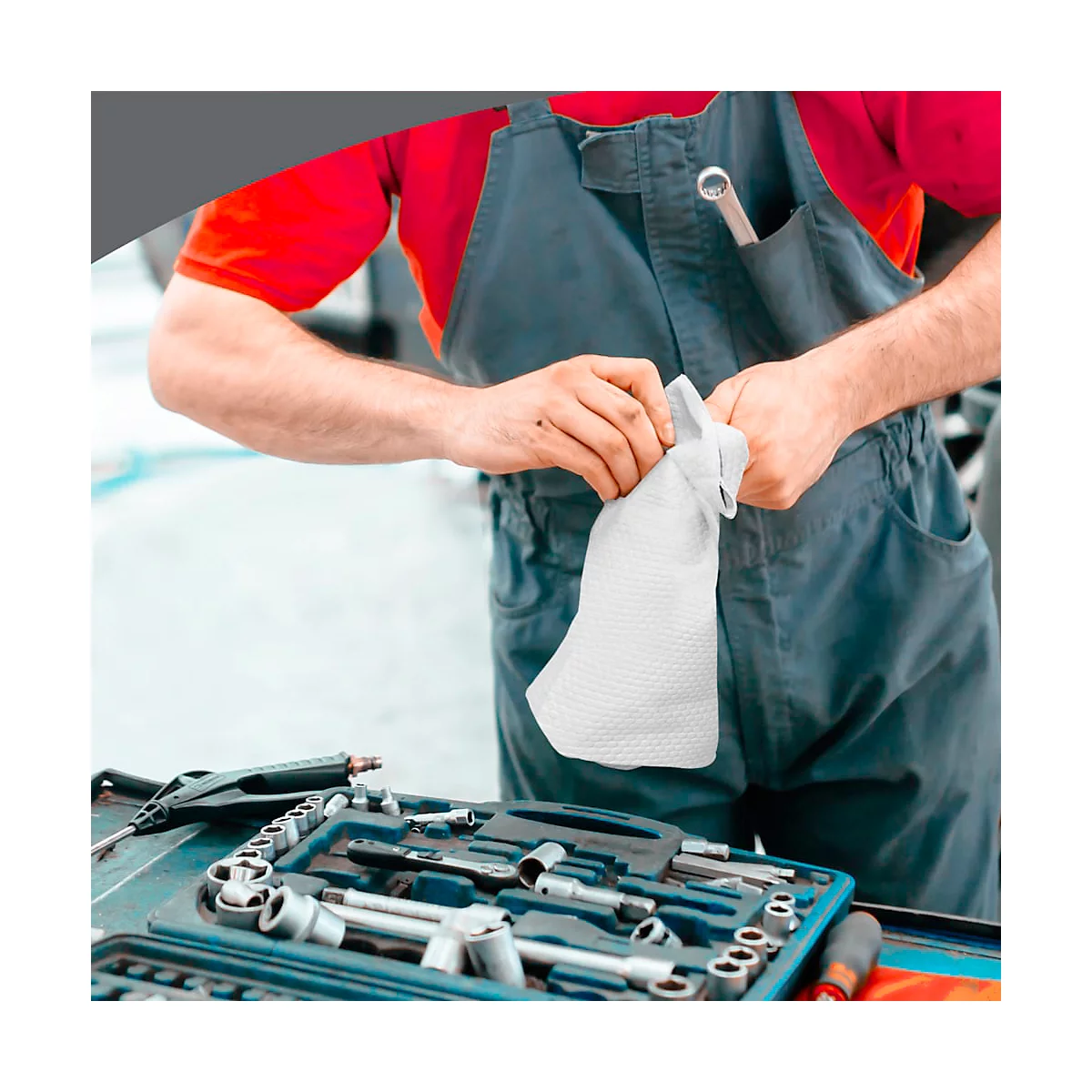 Ein Mechaniker hält einen weißen Stoffhandschuh. Werkzeugkasten und Overall im Hintergrund.