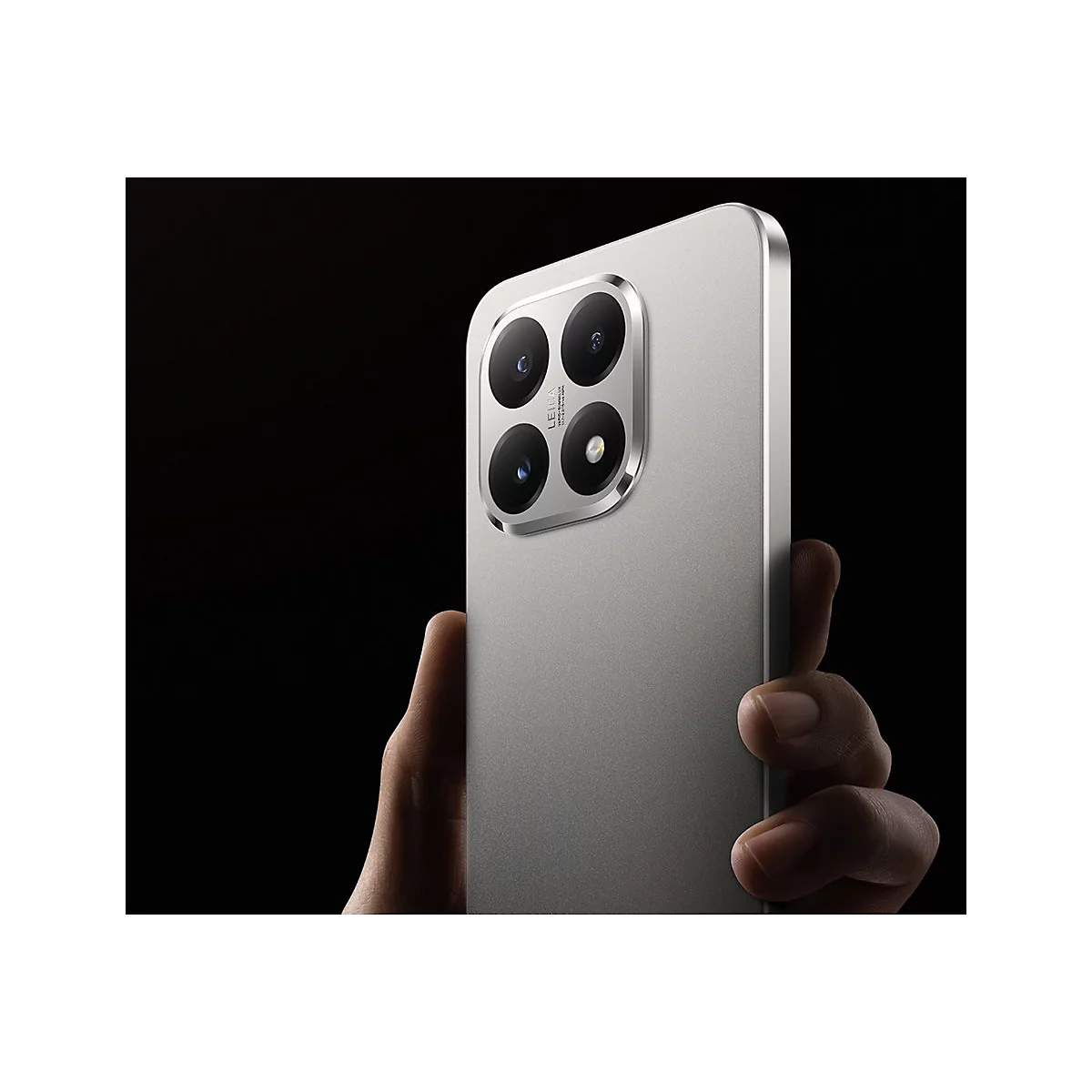 Hand hält silbernes Smartphone mit markantem quadratischem Leica-Kameramodul vor schwarzem Hintergrund.