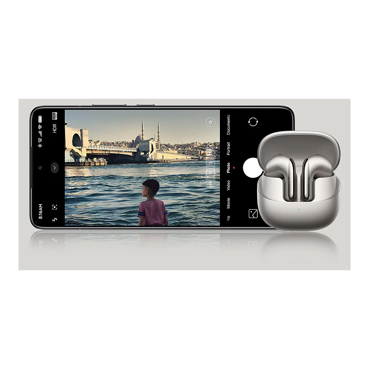 Smartphone zeigt ein Foto eines Jungen am Wasser. Rechts daneben befindet sich ein silbernes Ladecase mit In-Ear-KopfhÃ¶rern.