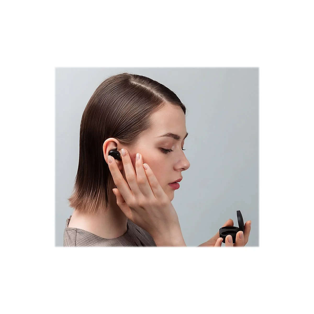 Junge Frau setzt einen schwarzen KopfhÃ¶rer in ihr Ohr ein. Sie hÃ¤lt die Ladebox in der Hand.