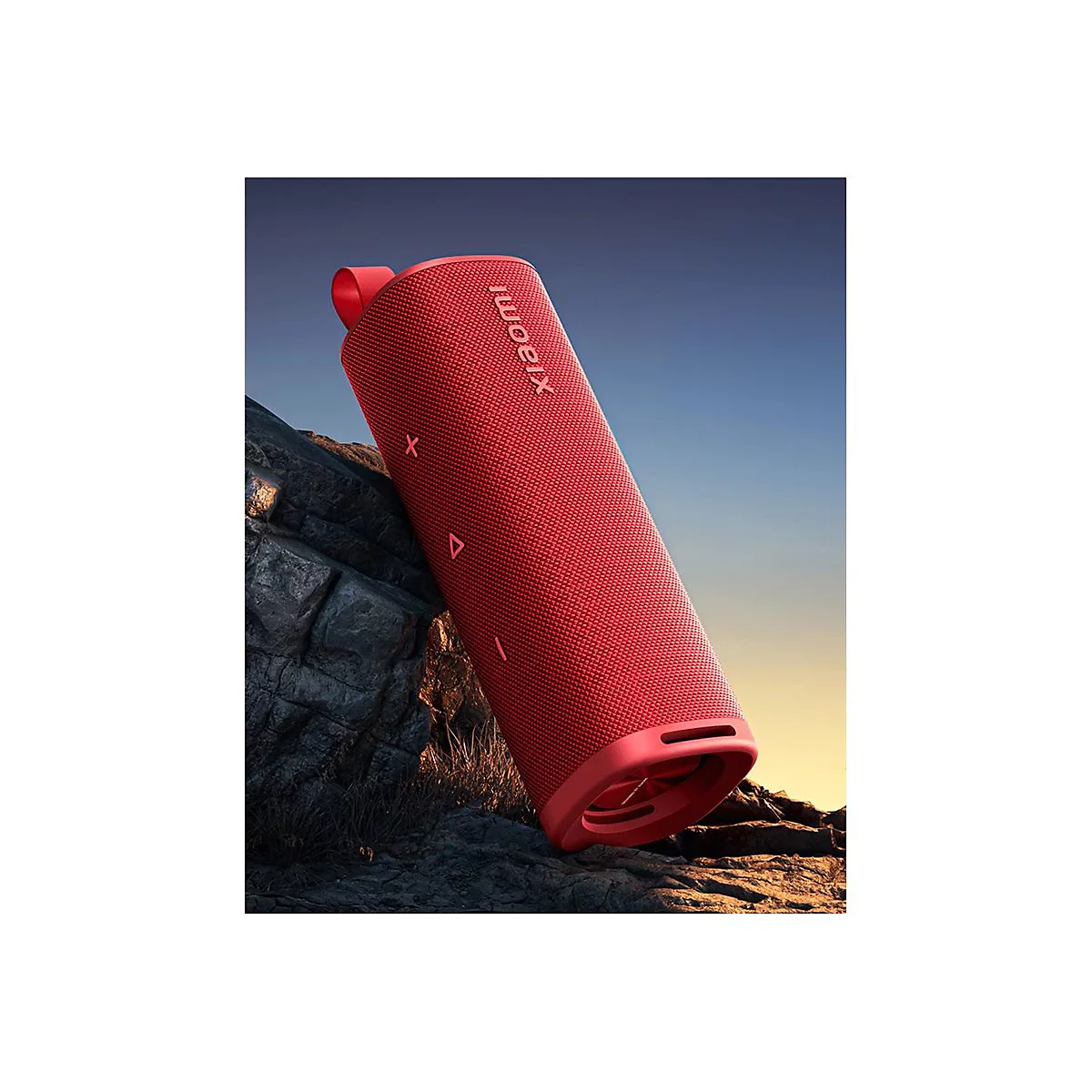 Roter zylinderförmiger Xiaomi-Lautsprecher lehnt vor Felsen in einer Dämmerungslandschaft.