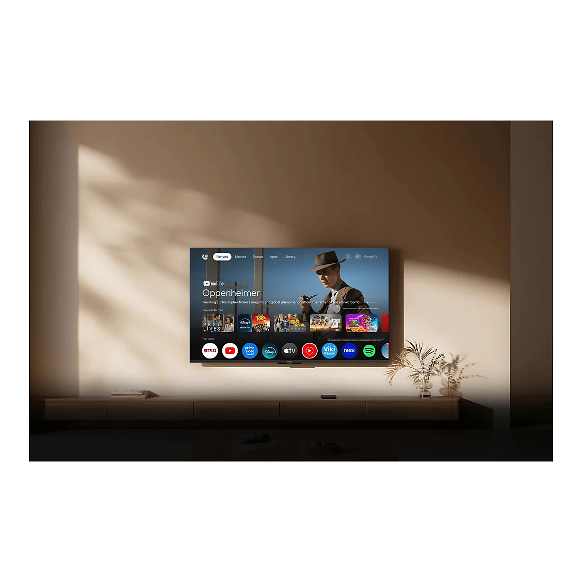 An der Wand hängender Fernseher mit Google TV Benutzeroberfläche und Filmauswahl in einem modern eingerichteten Raum.
