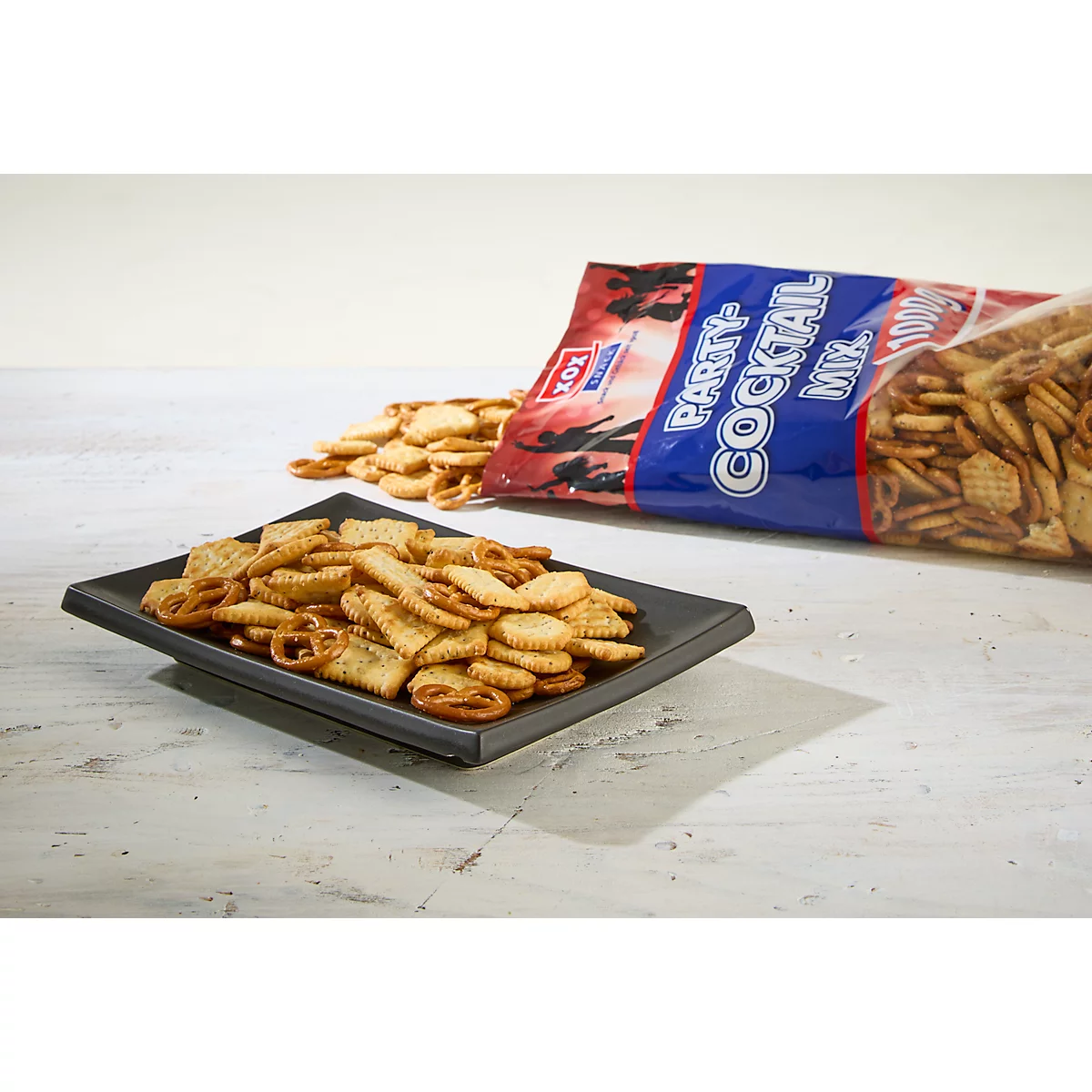 Ein Teller Party-Cocktail-Mix mit einer Tüte im Hintergrund. Einige Snacks liegen verstreut.