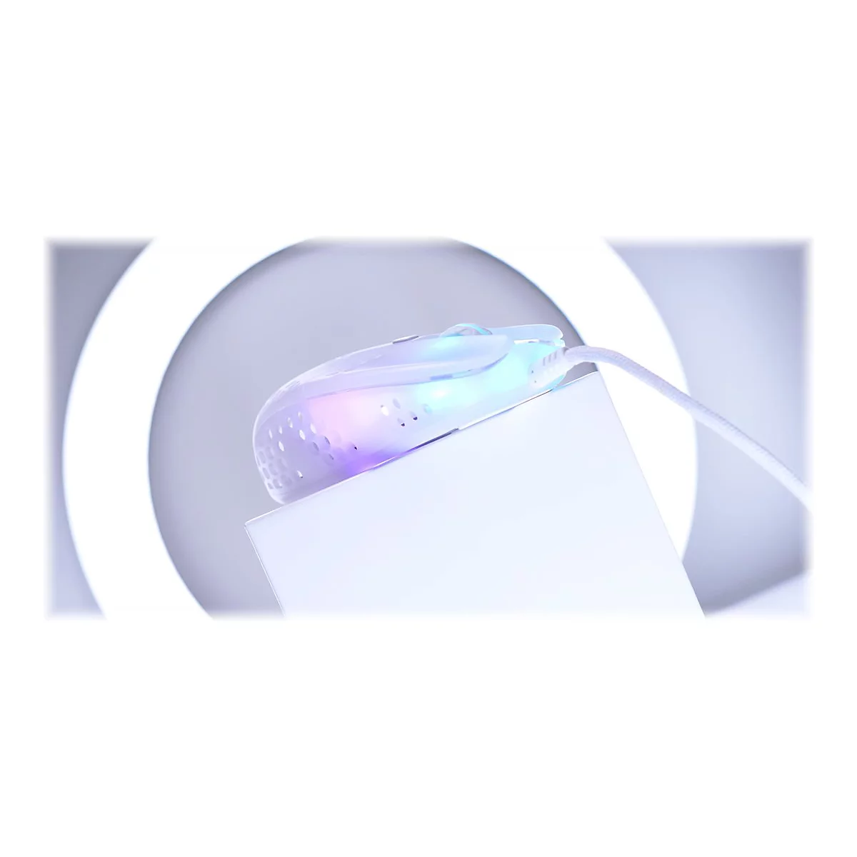 Eine transparente, beleuchtete Maus liegt auf einer weißen Oberfläche. Das Lichtspiel erzeugt eine Regenbogenfarben-Optik. Ein weißes Kabel ist angeschlossen.