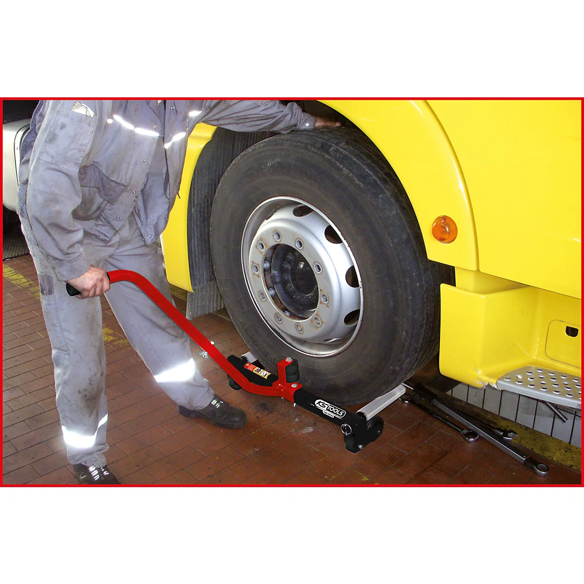 Ein Mechaniker benutzt ein rotes Werkzeug, um einen Reifen eines gelben Lkws zu wechseln.