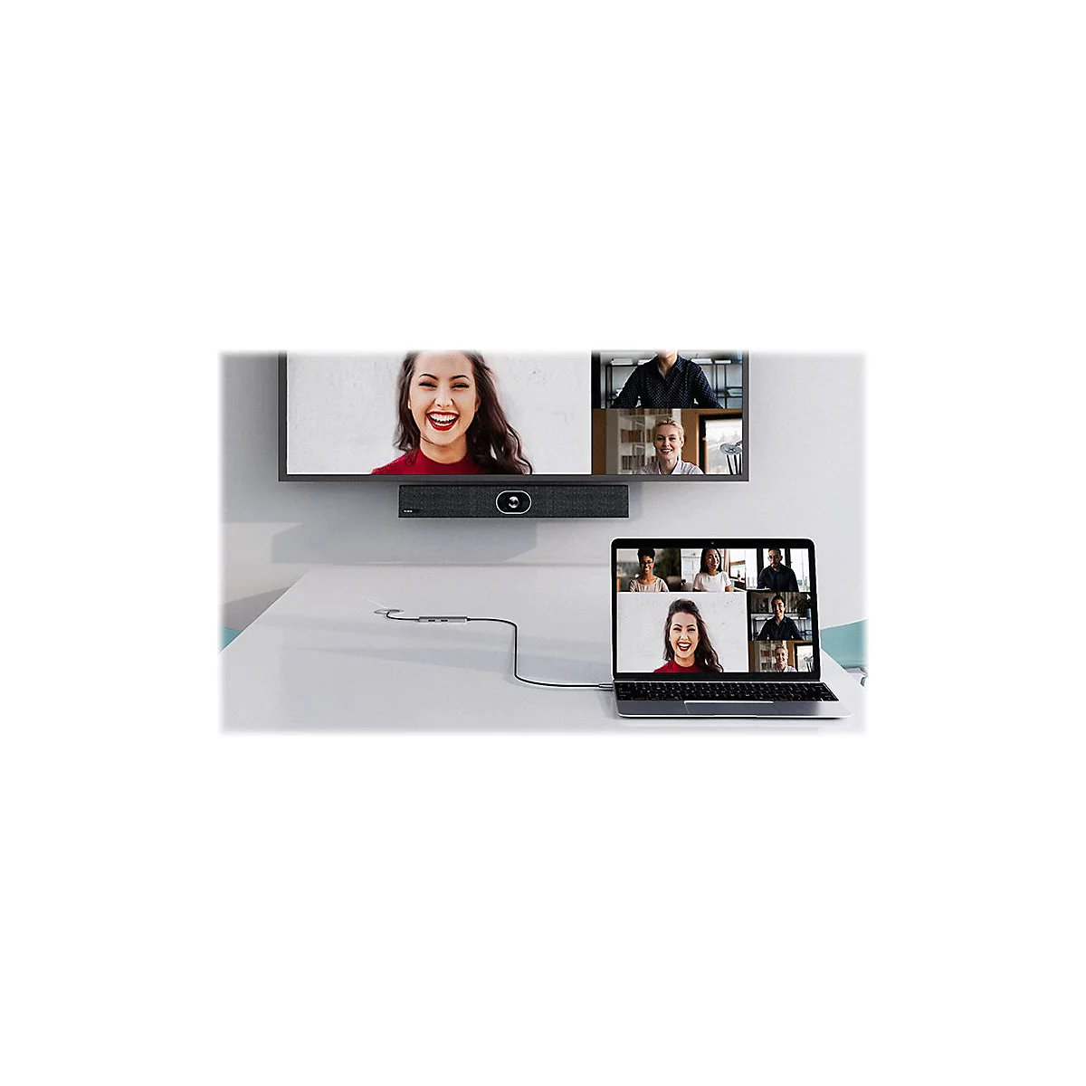 Frau in Videokonferenz, Blick auf einen Bildschirm. TV mit Lautsprecherleiste, Laptop mit Teilnehmern. Auf Tisch liegendes Kabel.