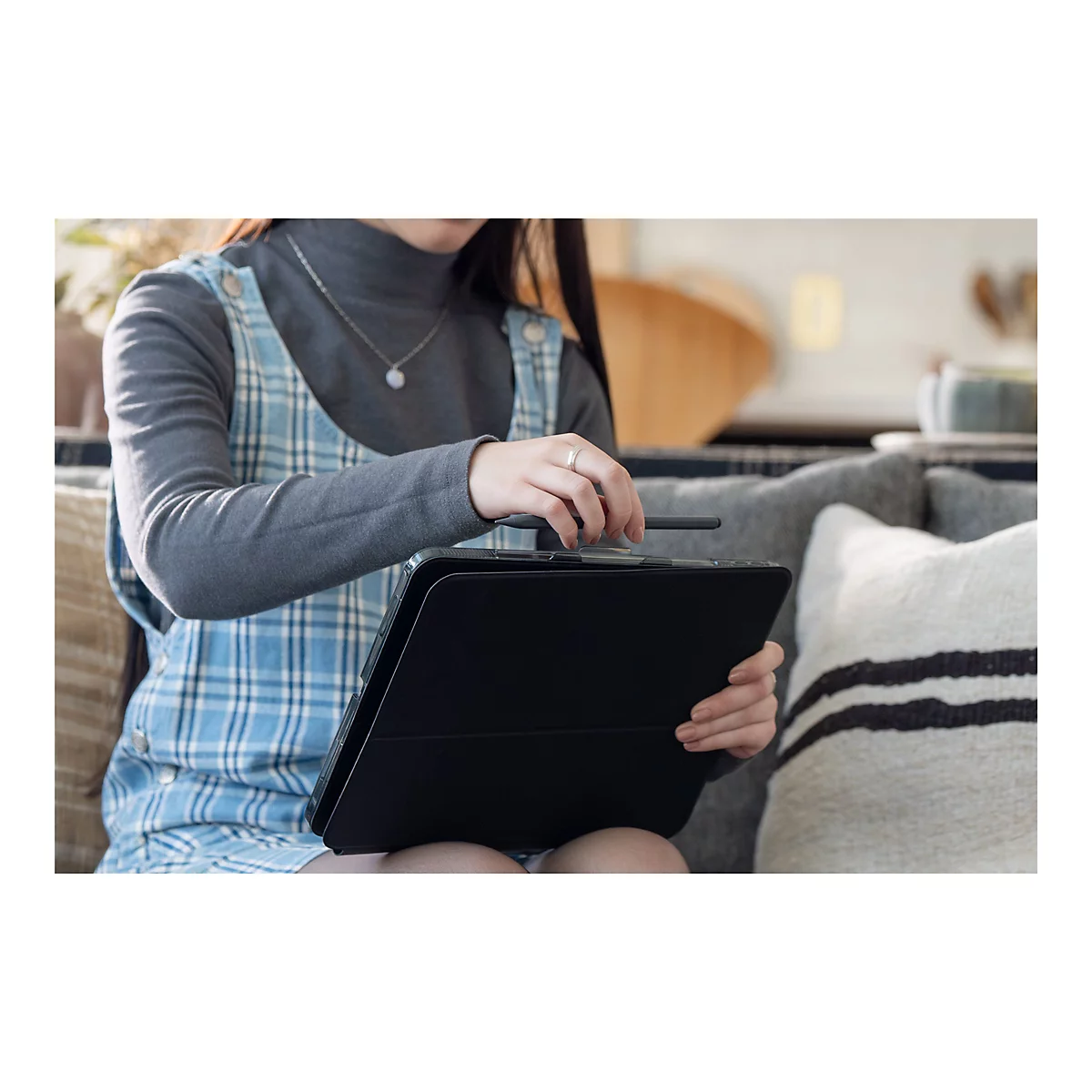 Eine Person hält ein schwarzes Tablet, daneben ein Stift. Sie trägt ein blau-weiß kariertes Kleid.