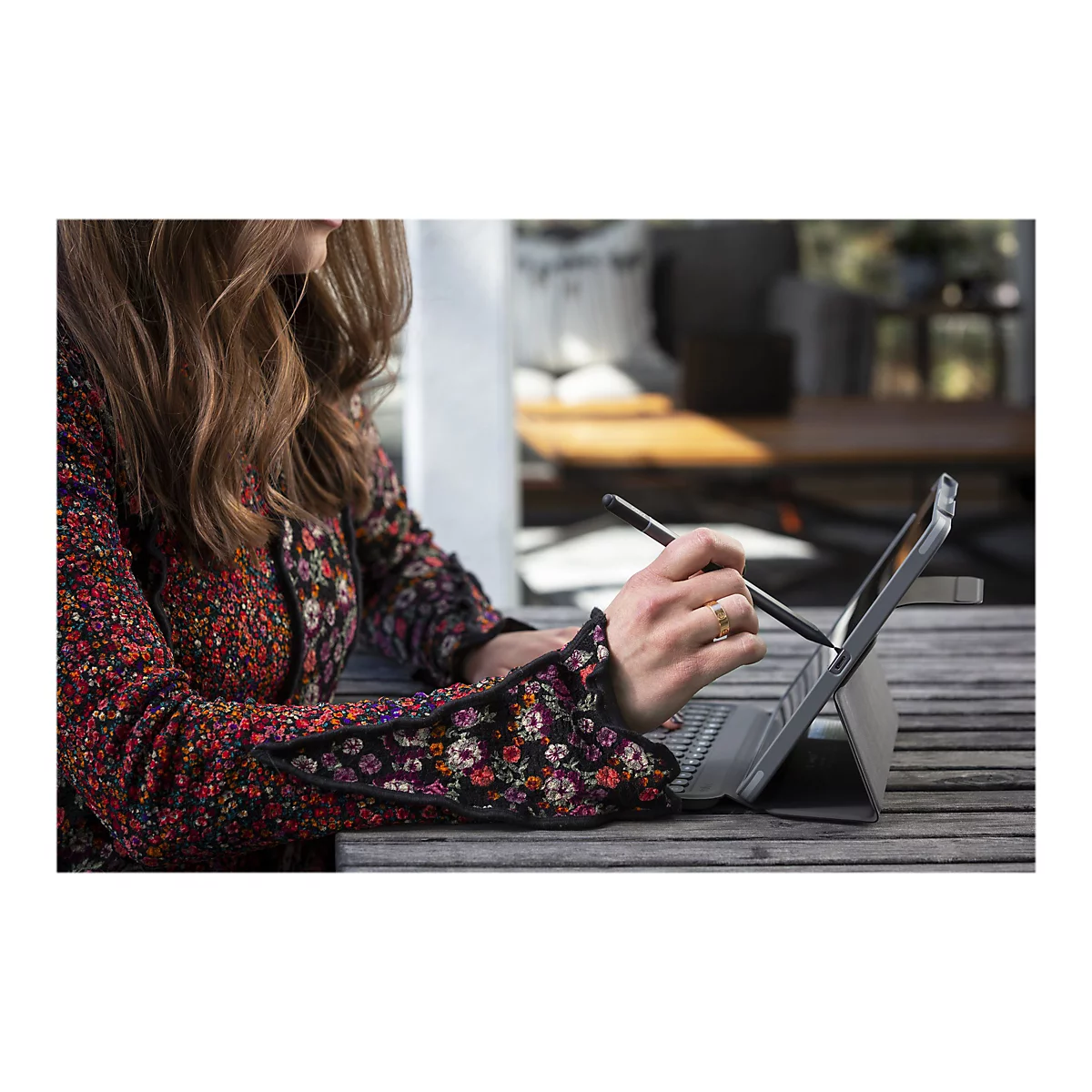 Une femme travaillant sur une tablette avec un stylet, portant un manteau fleuri et une bague en or.