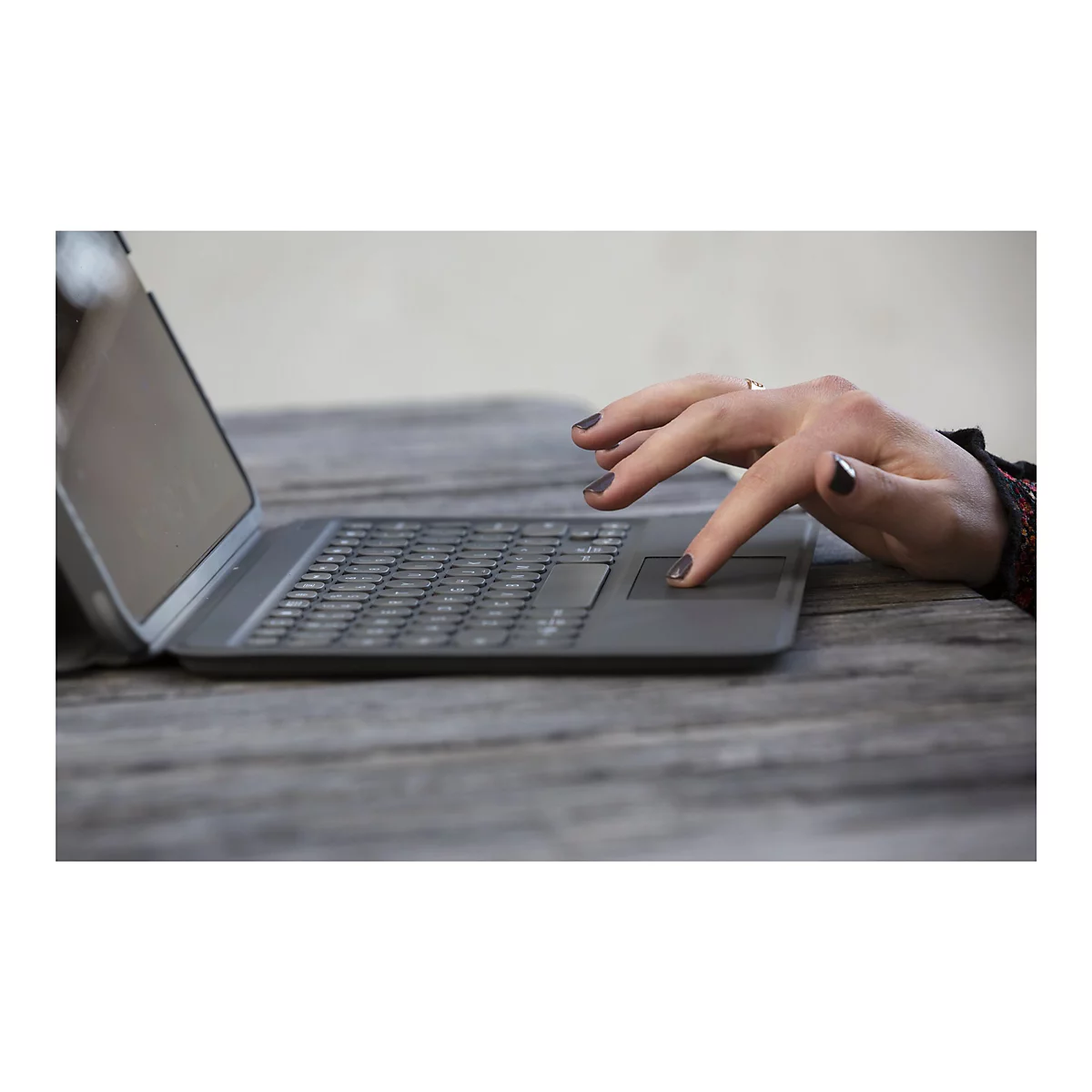 Une main tape sur un pavé tactile d'ordinateur portable. Le doigt avec du vernis à ongles foncé touche la surface.