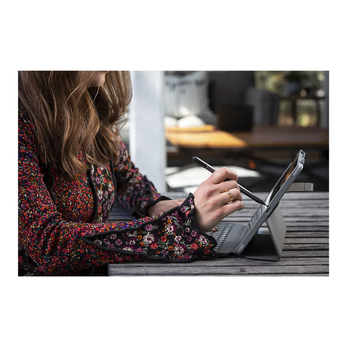 Personne écrivant sur une tablette avec un stylo. Elle porte une bague. Ses vêtements ont un motif floral.