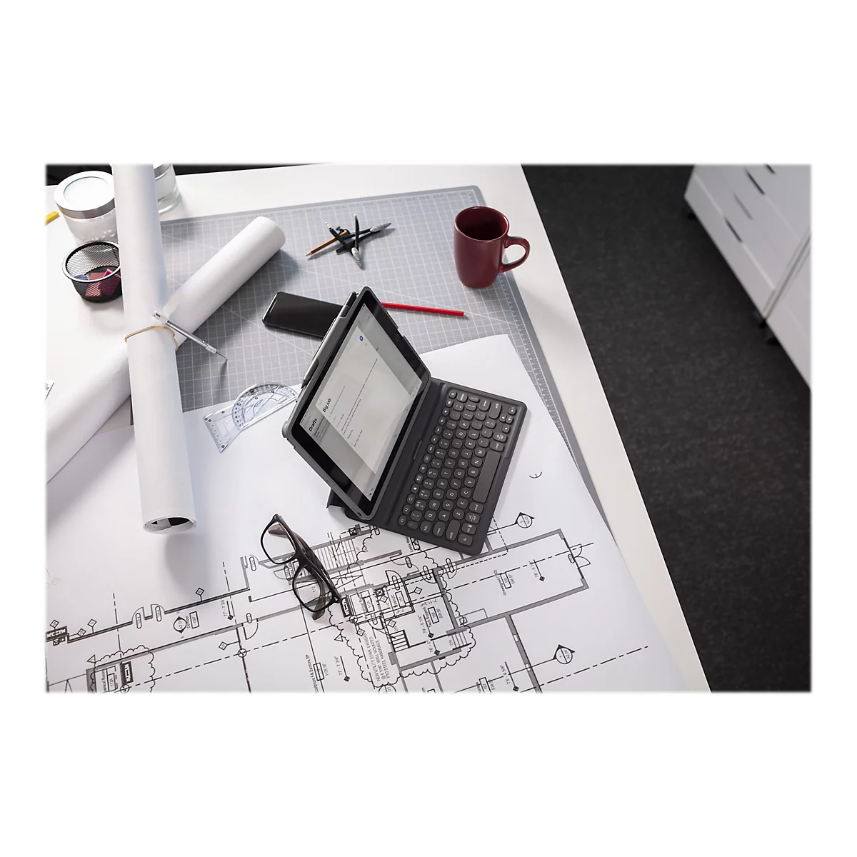 Ein Tablet mit angebrachtem Keyboard liegt auf einem Tisch. Auf dem Tablet-Bildschirm ist ein E-Mail-Entwurf zu sehen. Auf dem Tisch sind weitere Gegenstände zu sehen, darunter Baupläne, eine Tasse, eine Brille und Bürobedarf.