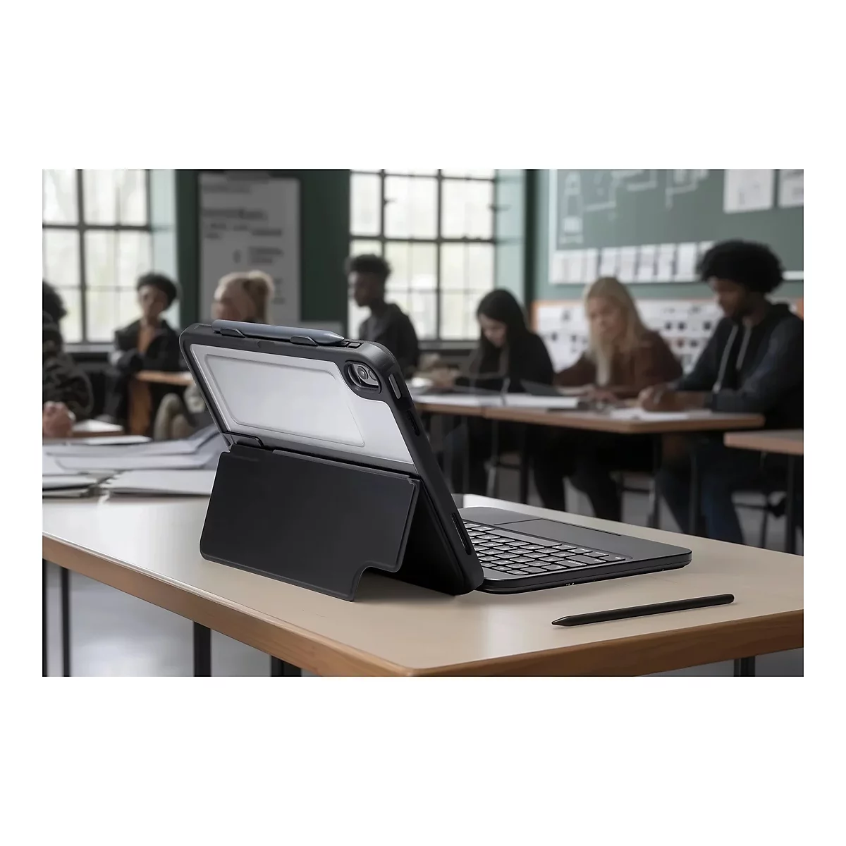 Ein Tablet mit Tastatur in einem Klassenzimmer. Auf einem Tisch liegen Stifte und Notizen. Im Hintergrund sitzen Schüler.